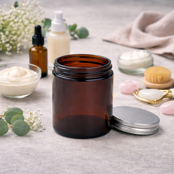 Amber glass cosmetic jar with an aluminium lid beside skincare products and eucalyptus