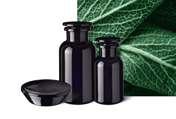 Two Miron violet glass apothecary jars with glass stoppers and a violet glass lid, beside a close-up of a green sage leaf
