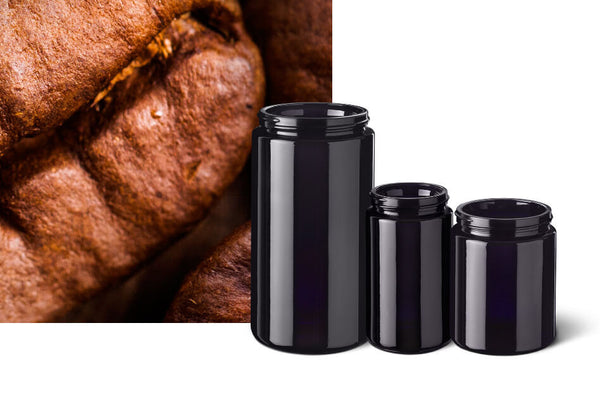 Three Miron violet glass wide neck jars in different sizes beside a close-up of a roasted coffee bean