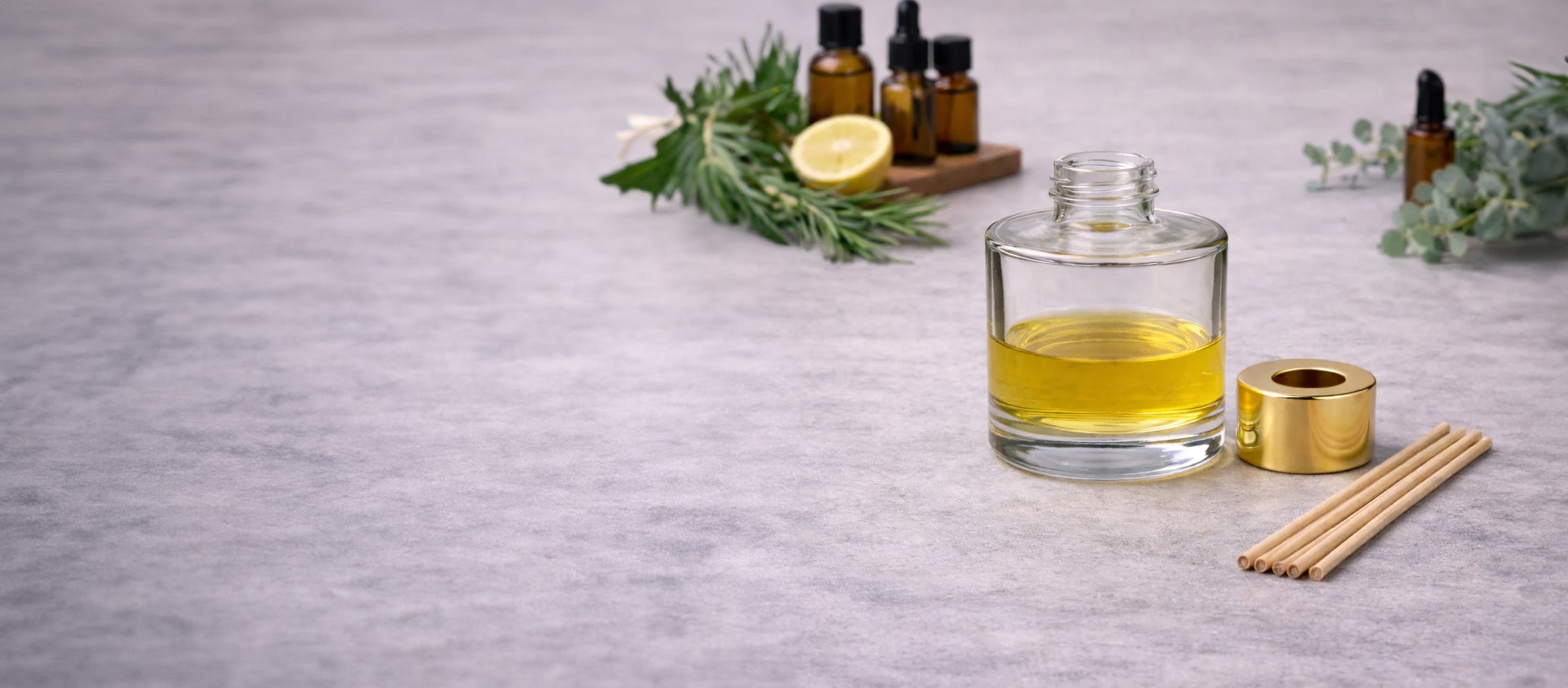 Glass bottle of oil with lemon, herbs, and candles on a gray surface