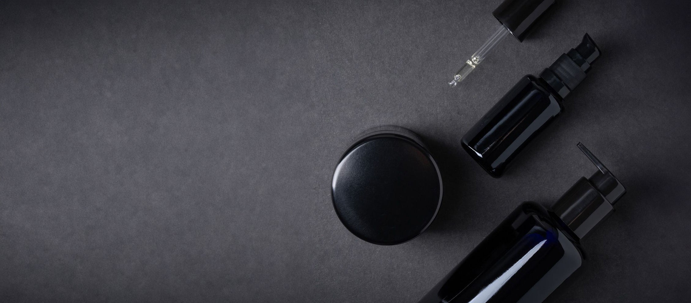 Black skincare bottles and containers on a dark textured background