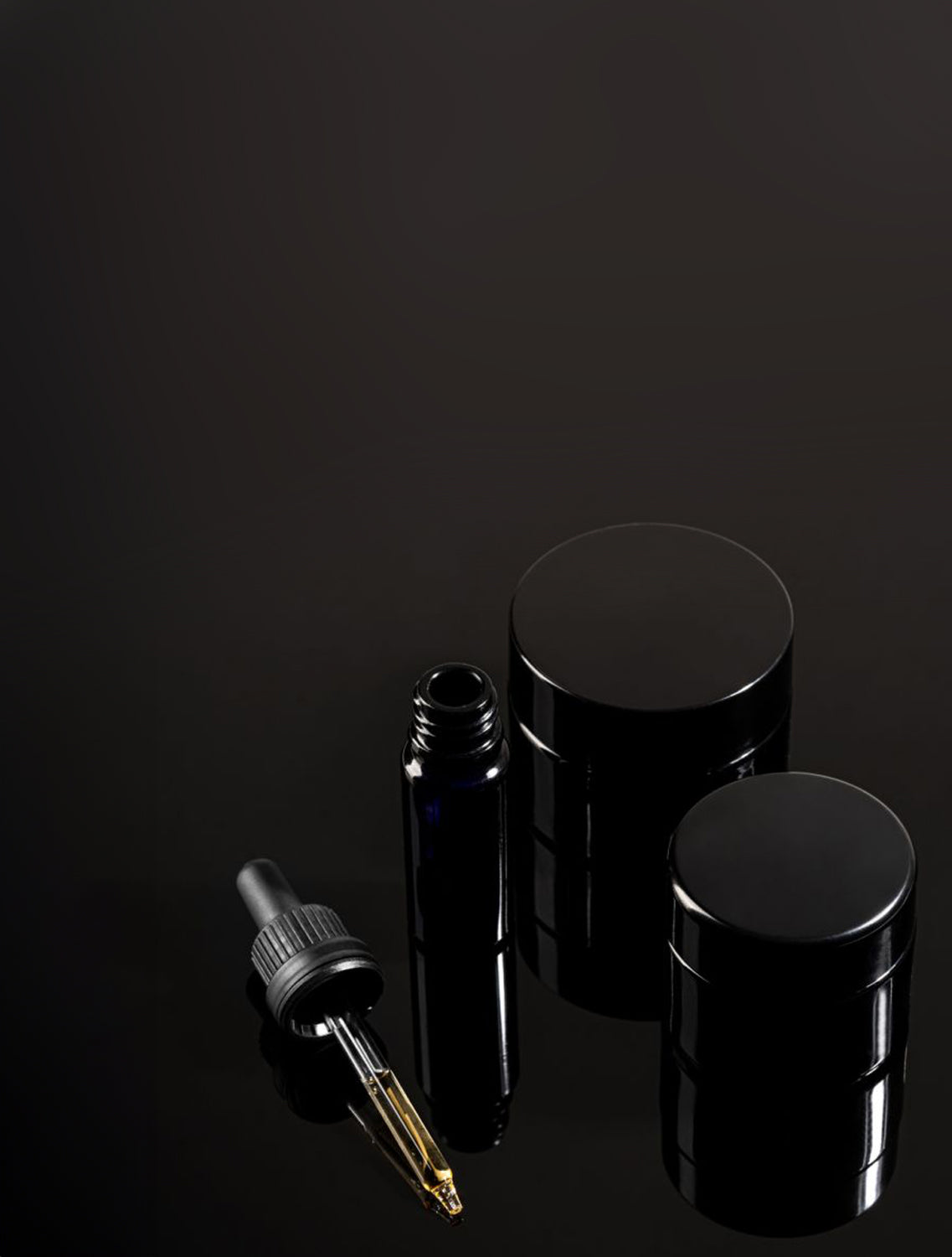 Set of black Miron glass containers with a dropper on a dark background